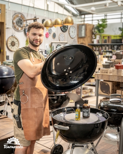 Un homme souriant présente un barbecue boule noir ouvert dans un magasin de jardinage, idéal pour la fête des pères.